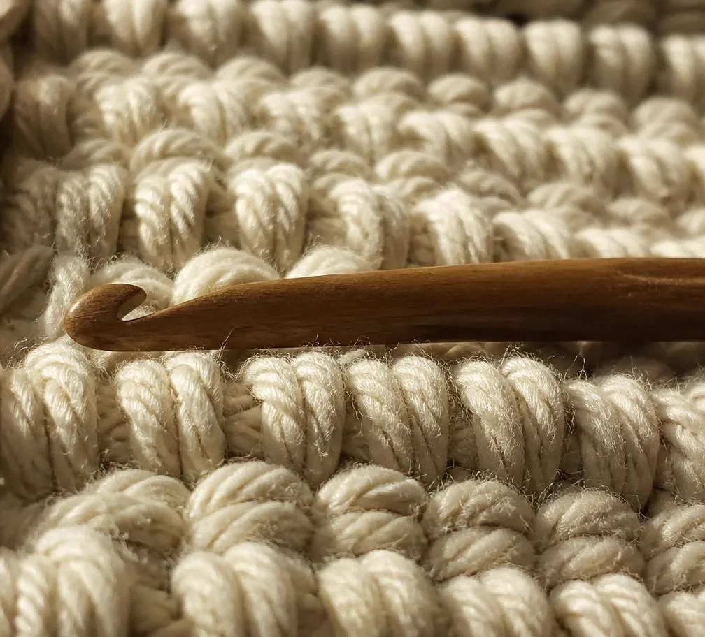 Close up of loomed cream stitches with a wooden hook