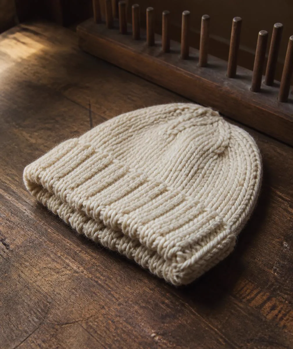 A finished cream loomed beanie beside wooden loom pegs