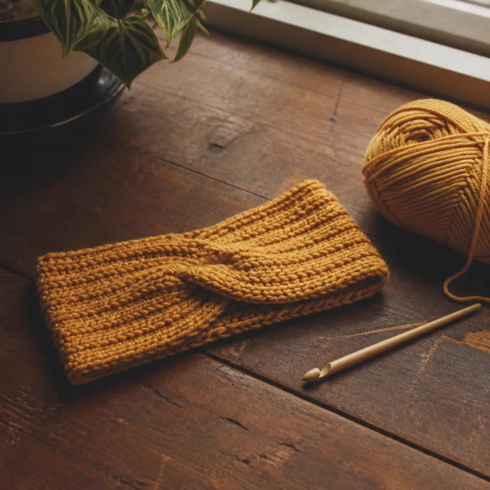 A mustard crocheted headband beside a hook and yarn